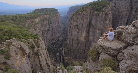 Tourist man sitting on the edge of the mountaing cliff against the backdrop of a gorge. Amazing Tazi Canyon ,Bilgelik Vadisi in Manavgat, Antalya, Turkey. Greyhound Canyon, Wisdom Valley.