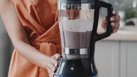 Mid-section tracking shot of unrecognizable young woman making delicious smoothie in blender in kitchen