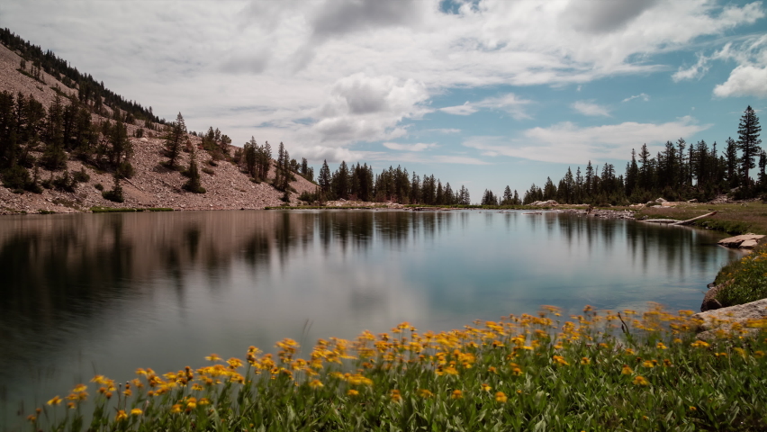 A time-lapse of clouds passing over Johnson Lake, an alpine lake in the Snake Range, located inside Great Basin National Park in Nevada, as seen on a summer day. Yellow flowers line the lakeshore. | Shutterstock HD Video #1084362454