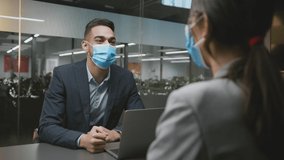 Business and preventive measures. Young man consultant putting on protective face mask and greeting woman client, sitting with laptop at office, slow motion - Powered by Shutterstock - Get 15% off with code: PIKWIZARD15