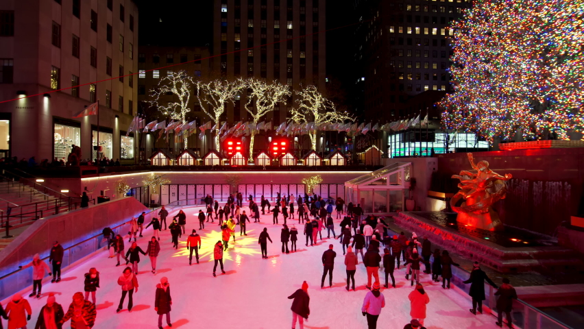NEW YORK, USA - DECEMBER 21, 2021: Ice skating rink near Rockfeller center. People have fun and good time ice skating. Christmas decorations. Night time