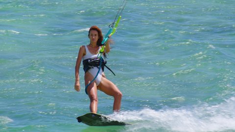 Beautiful girl kitesurfing in white swimsuit. Extreme kiteboarding in slow motion. Summer fun action sports.