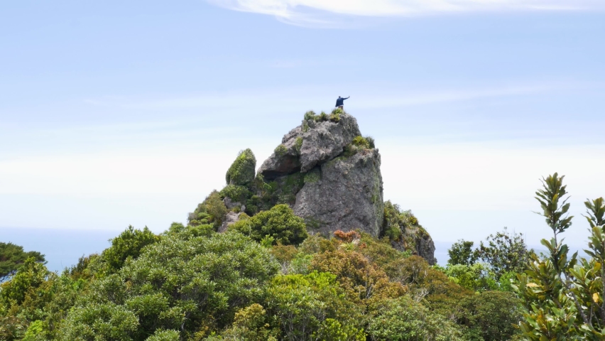 Person taking selfie photo on mountaintop of rock,enjoying success and view during sunny day - Blue Ocean in background - Te Whara Track,New Zealand