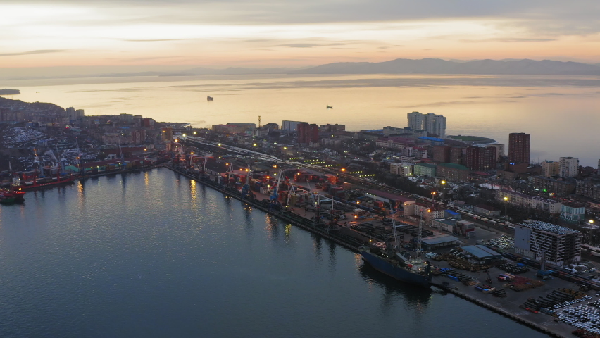 Drone view of the cargo terminal with port cranes at sunset. There are containers and cars on the quay. Freight shipping concept. Egersheld Peninsula, Vladivostok.