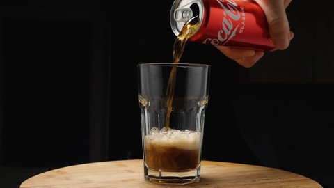 A man's hand from a can pours Coca-Cola into a highball glass. The camera flies around. Parallax effect. Dark background. Russia, Krasnodar, December 24, 2021