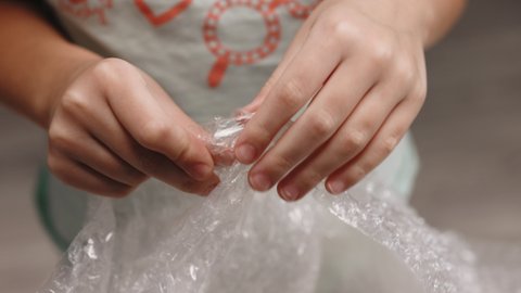 Little teenager girl bursts with her fingers the bubble wrap from the package. Bubble wrap replaces spinner, slime and pop it. Girl pressing the bubble wrapping. Stress concept