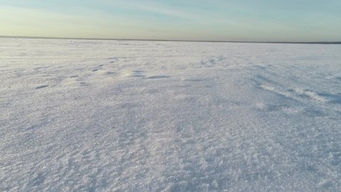 The drone flies over a snowy lake. Shiny snow flies around. The drone hovers over a snowy field. A hovercraft rides on a snow-covered lake.