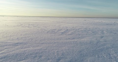 The drone flies over a snowy lake. Shiny snow flies around. The drone hovers over a snowy field. A hovercraft rides on a snow-covered lake.