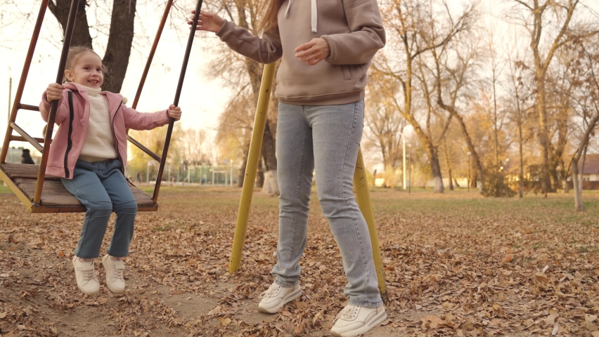 little kid swinging on a swing and laughing while flying up, an autumn playground, a happy family, a mother rolls child in city park, childhood dream to fly, smile at mom on a walk, play with a baby Royalty-Free Stock Footage #1084383889