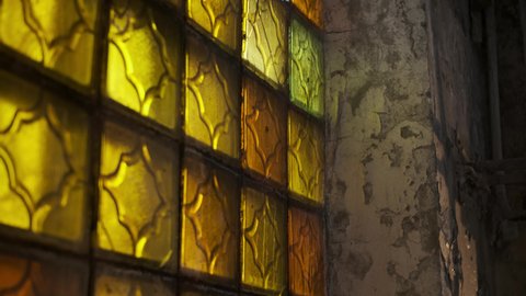 close up view of yellow stained glass windows in abandoned building with concrete walls. Light passes through yellow glass and enters interior of building.