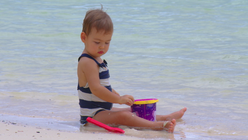 Young mother and her little daughter playing and relaxing on the sea beach with sand at summer vacation time. Happy family, parenthood concept