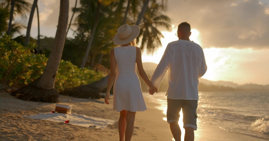 Back view couple of lovers walk along sandy beach enjoying tropical sunset havig good time together
