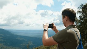 Blogger or vlogger recording video on smartphone, standing on high mountain top. Travel man with backpack making content for social media network with beautiful landscape on high view point.