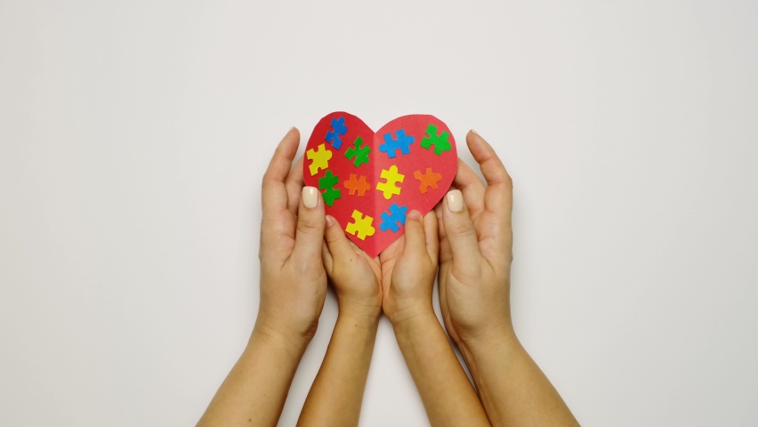 A child and a mother are holding a red heart with colorful puzzles inside - a symbol of autism. the concept of supporting families with children suffering from autism syndrome | Shutterstock HD Video #1084411060