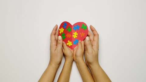 A child and a mother are holding a red heart with colorful puzzles inside - a symbol of autism. the concept of supporting families with children suffering from autism syndrome