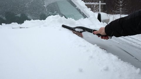 Person brushing fresh snow from car windows after snow storm blizzard. Morning routine difficulties of car owners in cold winter weather. Car window cleaning. Winter season. White snow. Vehicle care.