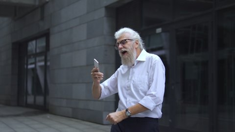 Healthy mature man having fun dancing outdoor to music from app on smartphone