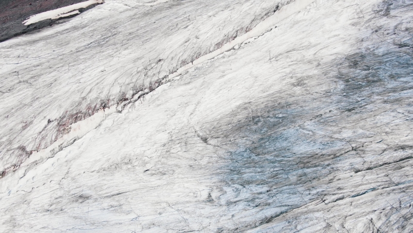 Large high grey cliffs with blue shadow rifts and big deep cracks covered with snow and black mineral products aerial view