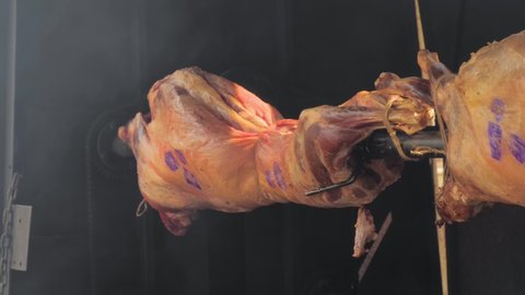 Process of cooking roasted whole ram carcasses on spit at summer outdoor food festival, market: close up. Professional cooking, preparation, cookery, gastronomy and street food concept