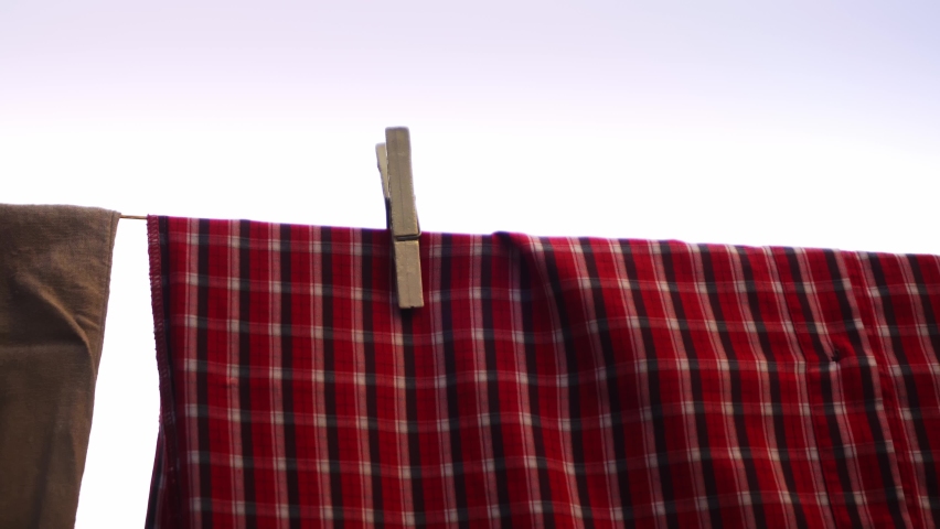 Red shirt is hanging on a wash line and drying after laundry filmed in closeup. Clothes are trembling by the wind on the clothesline after being cleaned up. It is hold by wooden pins. Theme of textile