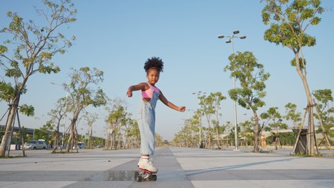 Little African child girl kid skating on skateboard at the park in the city. Happy cute preschool girl enjoy and having fun outdoor lifestyle practicing extreme sport skateboarding on summer vacation