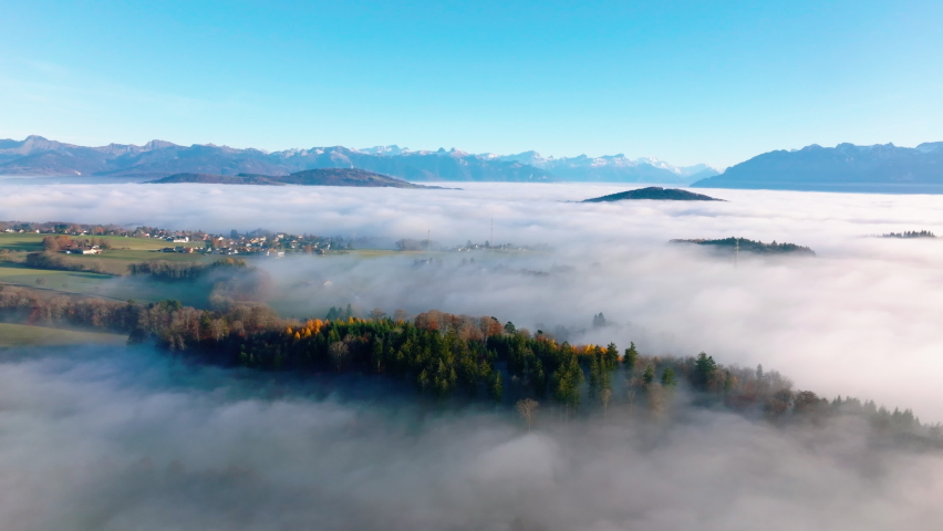 Misty woodlands and pastures on the Swiss Plateau with Savigny village in Vaud, Switzerland - aerial drone shot