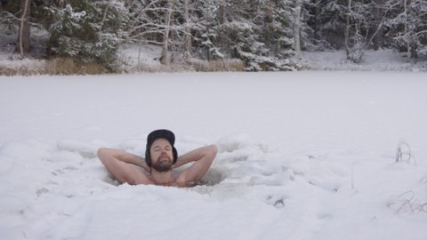 ZOOM OUT - An ice bather finishes his daily practice and steps out of his snowy ice hole