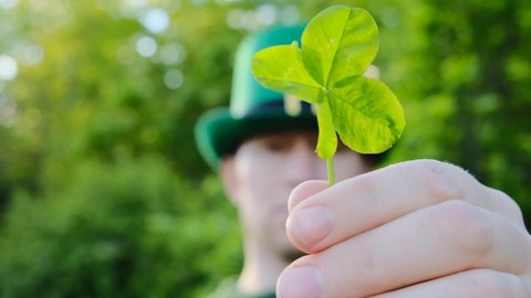 Saint Patrick.Four-leaf clover. Good luck symbol. clover leaf in the hand of a man in a green hat in a sunny spring garden.Irish traditional spring holiday
