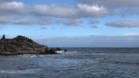 4K HD video of the tip of Lovers Point Park in Pacific Grove, California, waves coming in, people walking along the top of the rocks. Blue sky with white stormy clouds.