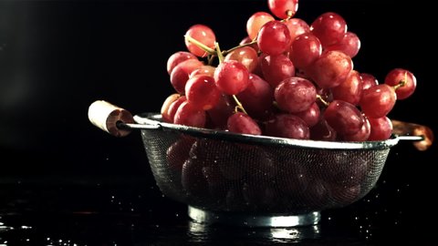 A colander with grapes falls on the table with drops of water. On a black background.Filmed is slow motion 1000 fps.