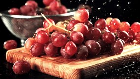 Water falls on the grapes on the cutting board. On a black background. Filmed is slow motion 1000 fps. High quality FullHD footage