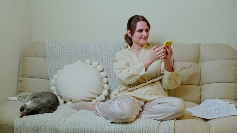 Woman musician with flute looking at mobile phone at home on sofa in living room