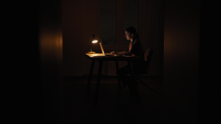 A woman at night under a lamp works from home in the dark. Evening time for work deadlines are burning deadlines. Royalty-Free Stock Footage #1084432585