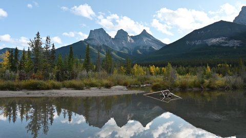 Scenery of Three Sisters Mountain in autumn forest with blue sky reflection on pond in Canmore at Banff national park, Canada