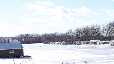 Cold winter day in Wisconsin with the sun shining on the frozen river. Houseboats closed up for the winter waiting for spring. Ice covering the water with snow drifts. 
