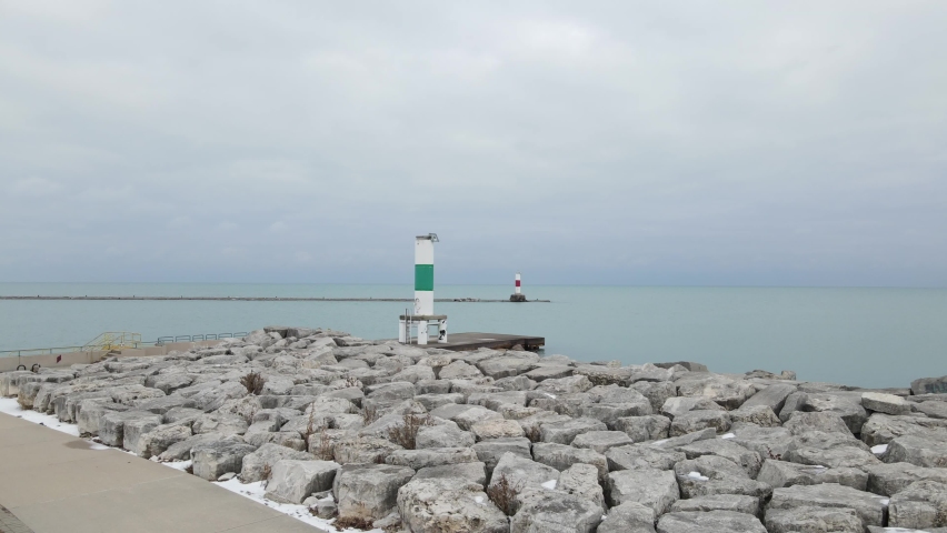 View of Lake Michigan harbor markers with a gray sky and calm waters. Concrete and boulders along the shoreline. Eastern shore of Wisconsin. 