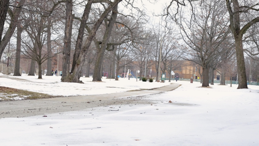 View down sidewalk of city park in Kenosha, Wisconsin. Snow covering grass. Bare tree branches lining sidewalk.