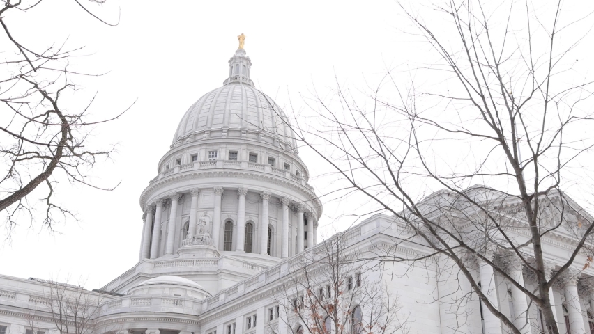 Exterior of Capitol in Madison Wisconsin. First level windows boarded up. Angles of the building. Granite exterior with ornate designs. Many ledges and balconies. 
