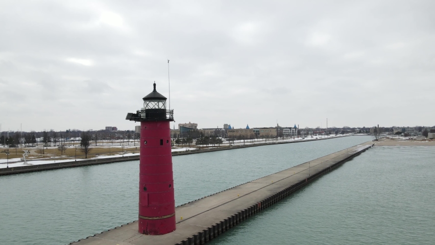 Lighthouse on pier in Kenosha, Wisconsin, with canal on each side. Cloudy sky and snow on ground. 