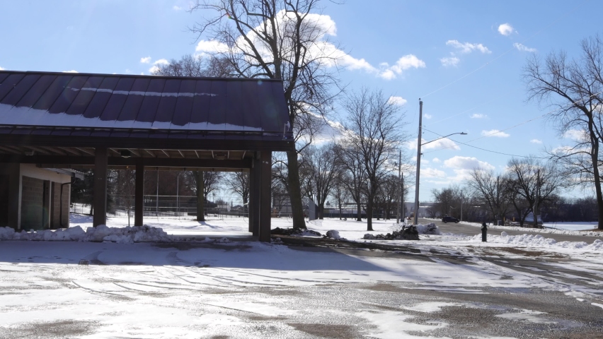Park shelter at end of road with fire hydrant in front. Curved road and vehicles parked on street. Bright blue sky and white clouds. Winter in Wisconsin with sun and shadows. 