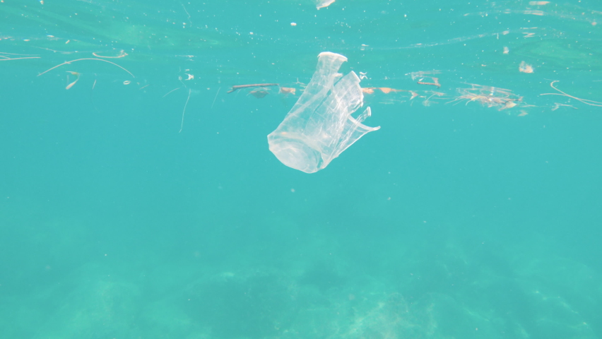 Trash garbage in the ocean waters, plastic cup littering sea, rubbish pollutes planet. Ecological problems, defending environment from pollution. Plastic trash on the surface of the water | Shutterstock HD Video #1084443421