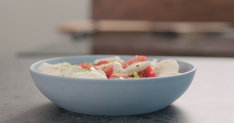 Slow motion orbit shot of man hands tries salad with frisee lettuce, tomatoes amd mozzarella in a blue bowl on kitchen countertop