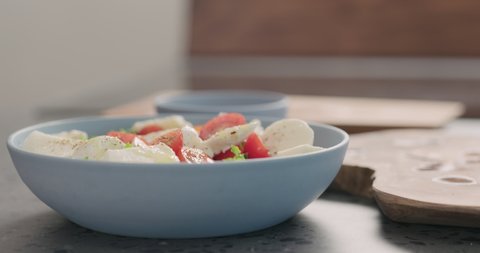 Slow motion orbit shot of salad with frisee lettuce, tomatoes amd mozzarella in a blue bowl on kitchen countertop