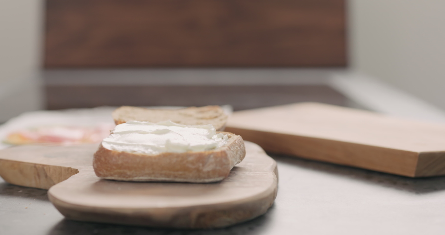 Slow motion orbit shot of man hands put smoked salmon on ciabatta with cream cheese to make a sandwich on wood board