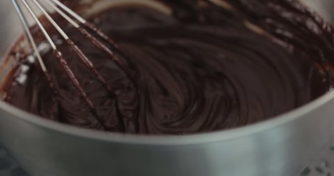 Slow motion handheld shot of whisking cream with chocolarte in steel bowl