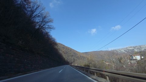 Slow car ride on a mountain road, passing by a mountain village. Autumn, blue clear sky