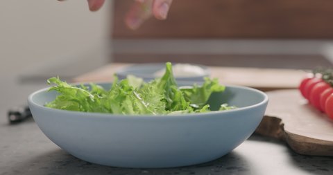 Slow motion orbit shot of man hands making salad with frisee lettuce, tomatoes amd mozzarella in a blue bowl on kitchen countertop