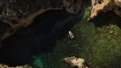 Aerial top view of tourist boat in Atlantic ocean with green water and cliff rocks in Ponta da Piedade, Algarve, Portugal
