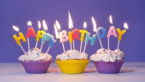 Happy Birthday Inscription Made of Burning Colorful Candles on Tasty Cupcakes isolated on purple background. Happy birthday video banner, slow motion.