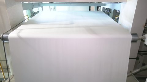 A beautiful smooth clean paper roll machine creating a continuous sheet of white freshly made paper for painting, wallpaper and wrapping. Industrial paper roll folds on industrial machinery.
